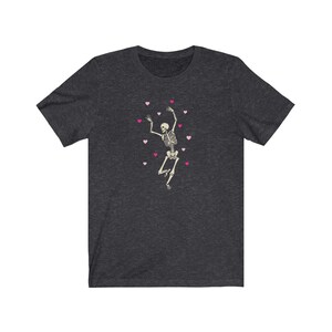 May include: A dark heather grey t-shirt with a skeleton dancing and surrounded by pink hearts.