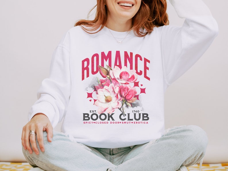 May include: White sweatshirt with the text "ROMANCE BOOK CLUB" in a maroon collegiate font. A floral graphic with pink and red flowers is centered below the text. The sweatshirt also has the text "EST. 1740 SPICY CLOSED DOORS SMUT EROTICA".