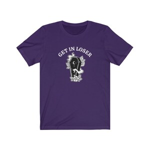 May include: Purple short-sleeved t-shirt with the text "GET IN LOSER" in white above a black and white illustration of a coffin with a crescent moon and flowers.