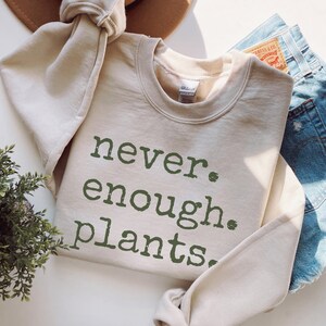 May include: A beige sweatshirt with the text "never. enough. plants." printed in green.