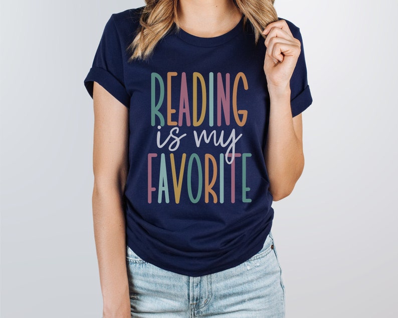 Puede incluir: Una camiseta azul marino con el texto "Reading is my favorite" en letras de colores.