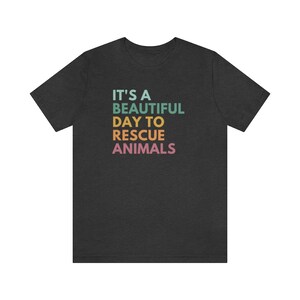 May include: A dark heather grey t-shirt with the text "It's a beautiful day to rescue animals" in rainbow colors.