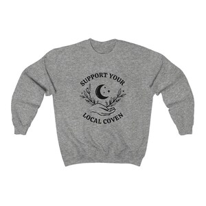 May include: Gray sweatshirt with a black graphic design that says "Support Your Local Coven" with a crescent moon, stars, and two hands holding the moon.