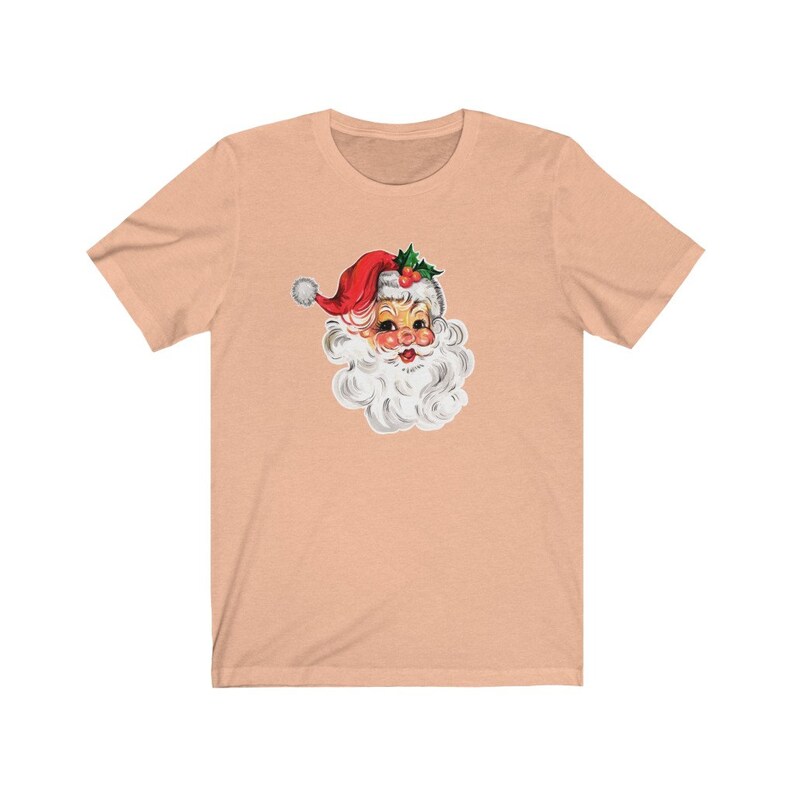 May include: A peach-colored t-shirt with a vintage illustration of Santa Claus's face. Santa is wearing a red hat with white trim and a white beard.
