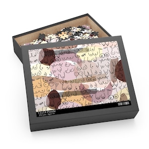May include: A black box with a 11x14 puzzle inside. The puzzle features a pattern of abstract breasts in various shades of pink, brown, and beige. The box has the text "11x14 Puzzle 252 pcs Ages 9+" printed on the bottom.