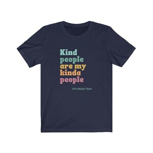 Pu&ograve; includere: Maglietta blu navy con il testo "Kind people are my kinda people" in colori arcobaleno. Il testo "5th Grade Team" &egrave; stampato sotto il testo principale.