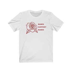 May include: White t-shirt with a red rose graphic and the text "BABES SUPPORT BABES" printed on the front.