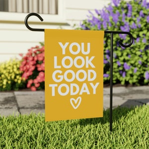 May include: A yellow garden flag with white text that reads "YOU LOOK GOOD TODAY" with a small white heart at the bottom.