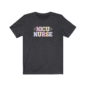 Peut inclure: Un t-shirt gris fonc&eacute; chin&eacute; avec le texte "NICU NURSE" en lettres color&eacute;es. Les lettres sont dans un style de police r&eacute;tro avec un sch&eacute;ma de couleurs rose, jaune et bleu.