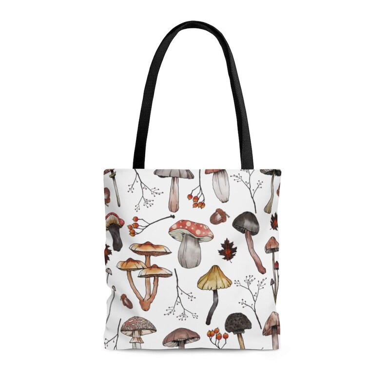 May include: White tote bag with a repeating pattern of watercolor mushrooms in shades of brown, red, and white. The mushrooms are of various shapes and sizes, and some have stems.