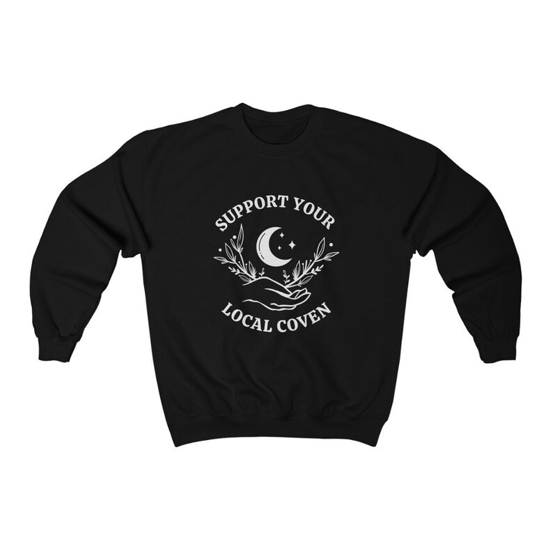 May include: Black sweatshirt with a white graphic design featuring a crescent moon, stars, and two hands holding a sprig of leaves. The text "Support Your Local Coven" is printed below the graphic.
