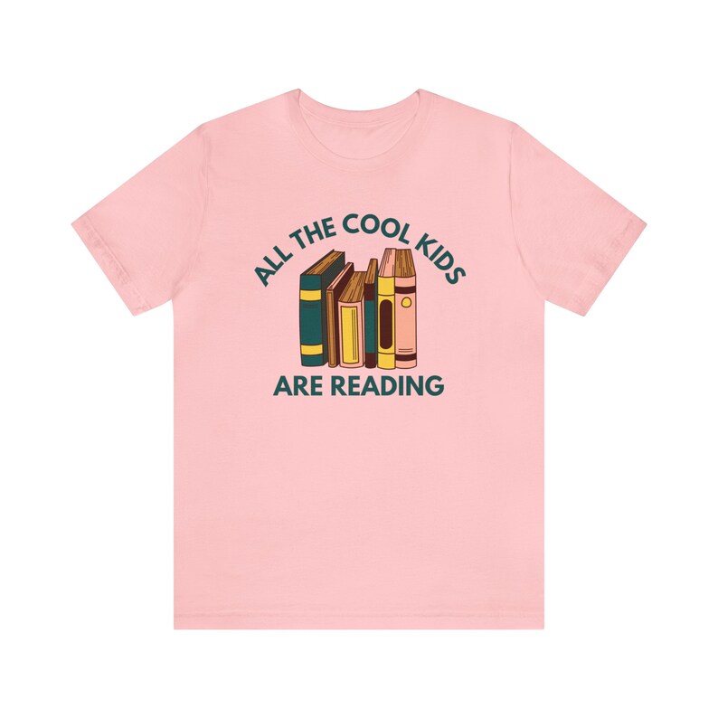 Puede incluir: Camiseta rosa con un gr&aacute;fico de una pila de libros y el texto "All the cool kids are reading."