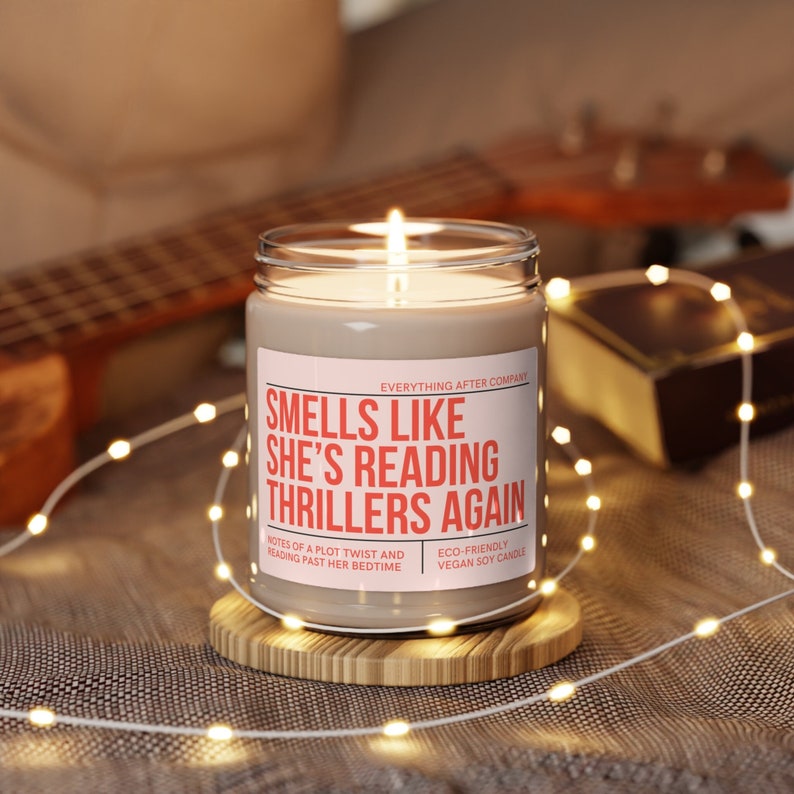 May include: A beige soy candle with a white label that reads "Smells Like She's Reading Thrillers Again". The label also includes the text "Everything After Company", "Notes of a plot twist and reading past her bedtime", and "Eco-friendly vegan soy candle".
