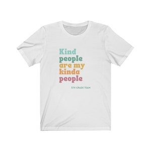 Pu&ograve; includere: Maglietta bianca con il testo "Kind people are my kinda people" in colori arcobaleno. Il testo "5th Grade Team" &egrave; stampato in un carattere pi&ugrave; piccolo sotto il testo principale.