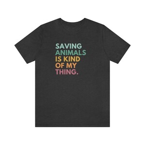 Puede incluir: Camiseta gris oscuro con el texto "SAVING ANIMALS IS KIND OF MY THING" en turquesa, verde, amarillo, naranja y rosa. La camiseta est&aacute; hecha de un material suave y es adecuada para uso casual.