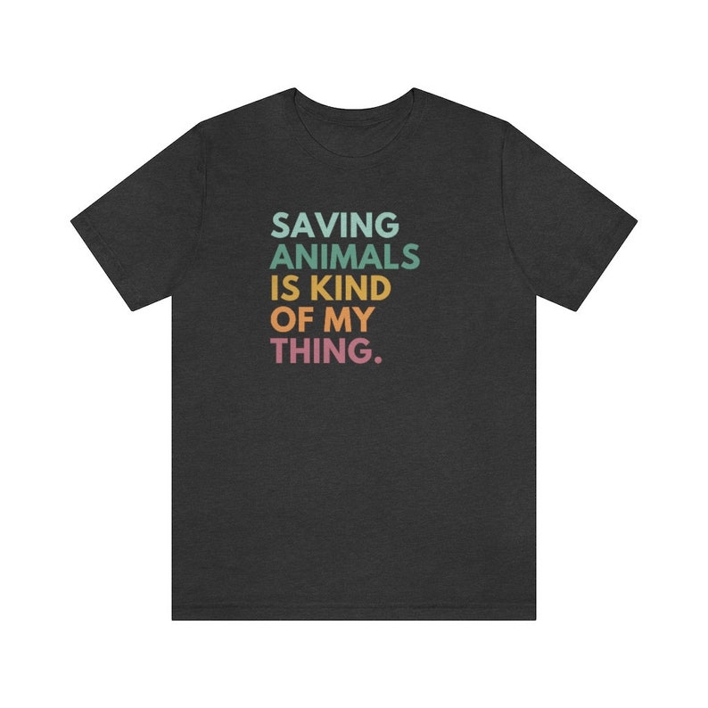 Puede incluir: Camiseta gris oscuro con el texto "SAVING ANIMALS IS KIND OF MY THING" en turquesa, verde, amarillo, naranja y rosa. La camiseta est&aacute; hecha de un material suave y es adecuada para uso casual.