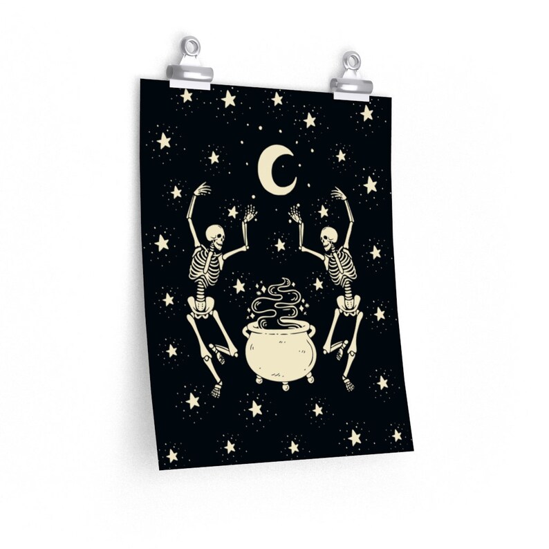 May include: A rectangular wall poster featuring a black background with a cream-colored crescent moon and scattered stars. Two skeletons are positioned on either side of a central steaming cauldron, with their arms raised toward the moon.