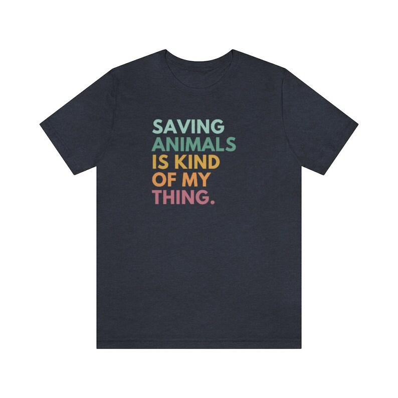 Puede incluir: Camiseta azul marino con la frase "SAVING ANIMALS IS KIND OF MY THING." en verde azulado, verde, amarillo, naranja y rosa. La camiseta tiene cuello redondo y es de tejido suave.