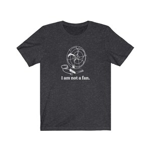 Peut inclure: Un t-shirt gris fonc&eacute; chin&eacute; avec un contour blanc d'un ventilateur vintage et le texte "Je ne suis pas un fan."