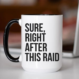 May include: White ceramic mug with a black handle and interior. The mug features the text "SURE, RIGHT AFTER THIS RAID" in bold black letters. The mug is on a white surface.