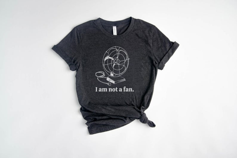 Peut inclure: Un t-shirt gris fonc&eacute; avec un graphique blanc d'un ventilateur vintage et le texte "Je ne suis pas un fan."