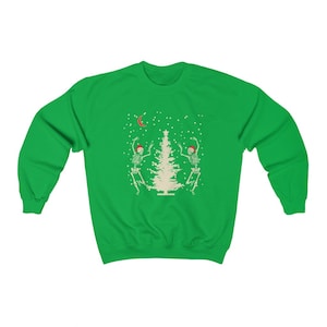 May include: Green Christmas sweatshirt with a white Christmas tree and two skeletons wearing Santa hats dancing around it. The skeletons are white with black outlines. There is a crescent moon and snowflakes in the background.