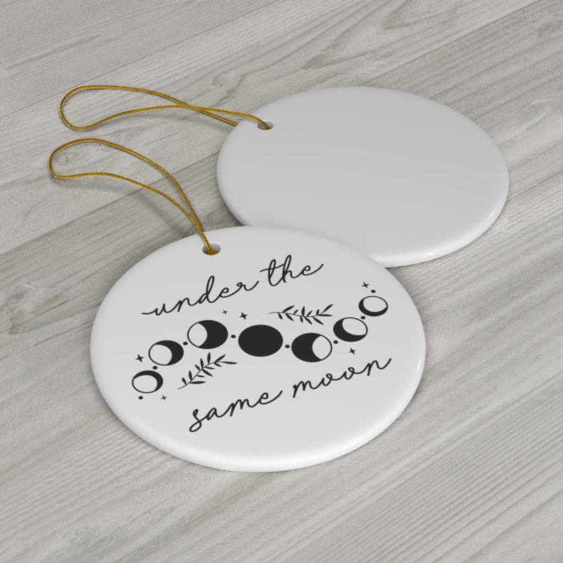 May include: White ceramic ornament with a black and white moon phase design and the text "under the same moon".