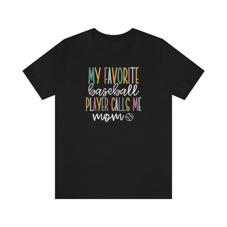 Op de afbeelding: Zwart T-shirt met de tekst "MY FAVORITE baseball PLAYER CALLS ME mom" in kleurrijke, speelse letters. Een honkbalafbeelding is inbegrepen. Het shirt is gemaakt van een zacht materiaal.