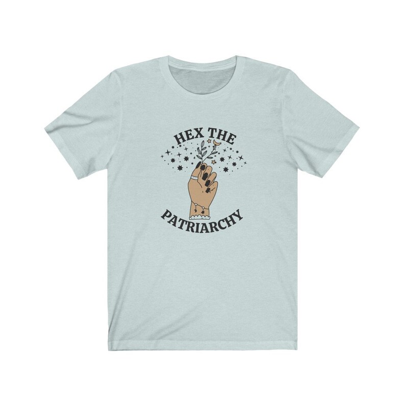 May include: Light blue t-shirt with the text "HEX THE PATRIARCHY" above an illustration of a hand holding a sprig of leaves and stars. The hand has black nail polish and a ring. The shirt is a short-sleeved crew neck.