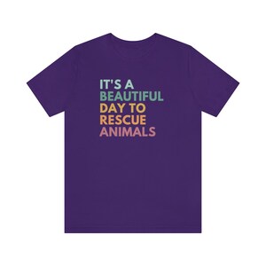 May include: Purple t-shirt with the text "It's a beautiful day to rescue animals" in rainbow colors.