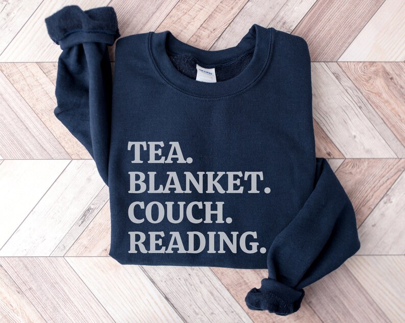 May include: A navy blue sweatshirt with the text "TEA. BLANKET. COUCH. READING." printed in white.
