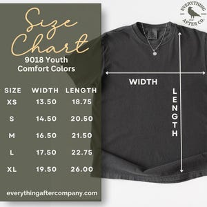 May include: A charcoal grey short-sleeve t-shirt displayed with a size chart overlay. The chart lists youth sizes XS through XL with width and length measurements in inches ranging from 13.50 to 26.00. A silver necklace rests on the shirt collar.