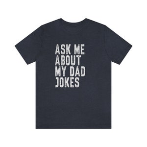 K&ouml;nnte beinhalten: Ein dunkelblaues T-Shirt mit dem Text "ASK ME ABOUT MY DAD JOKES" in wei&szlig;er, abgenutzter Schrift.