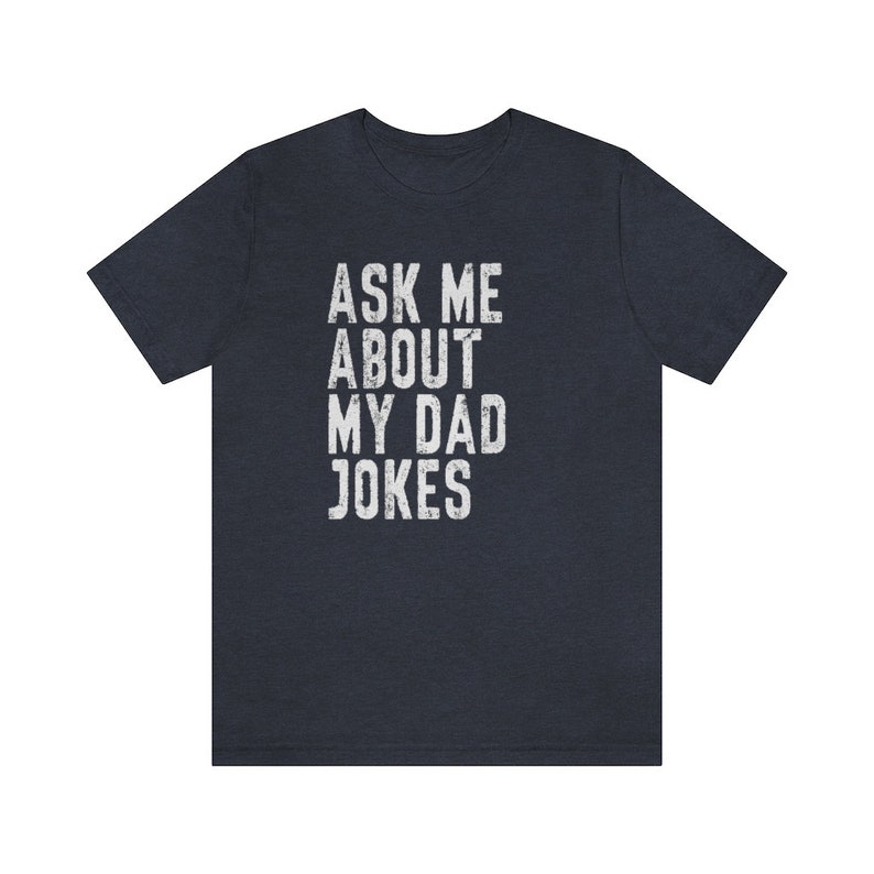 K&ouml;nnte beinhalten: Ein dunkelblaues T-Shirt mit dem Text "ASK ME ABOUT MY DAD JOKES" in wei&szlig;er, abgenutzter Schrift.