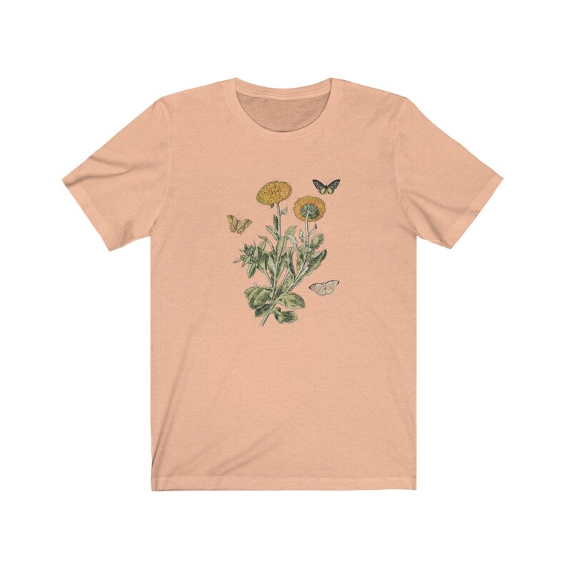 May include: A peach-colored t-shirt with a vintage botanical illustration of a yellow flower with green leaves and butterflies.