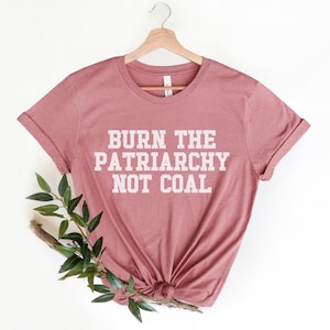 May include: A dusty rose colored t-shirt with the text "BURN THE PATRIARCHY NOT COAL" printed in white.