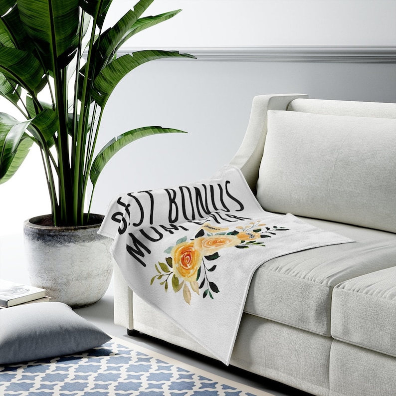 May include: White throw blanket with the text "Best Bonus Mum Ever" in black lettering and a floral design with yellow and green flowers.