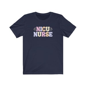Peut inclure: Un t-shirt bleu marine avec le texte "NICU NURSE" en lettres color&eacute;es. Les lettres sont dans une police de caract&egrave;res de style r&eacute;tro avec un sch&eacute;ma de couleurs rose, jaune et bleu.