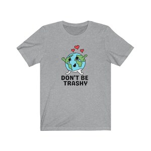 May include: A grey t-shirt with a cartoon Earth character, coloured blue and green, with a smiling face, arms, legs, and hearts above it. The text "DON'T BE TRASHY" is printed below the Earth. The t-shirt is a casual wear item.