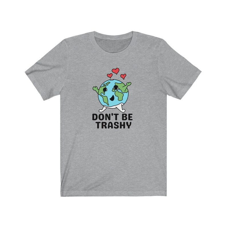 May include: A grey t-shirt with a cartoon Earth character, coloured blue and green, with a smiling face, arms, legs, and hearts above it. The text "DON'T BE TRASHY" is printed below the Earth. The t-shirt is a casual wear item.