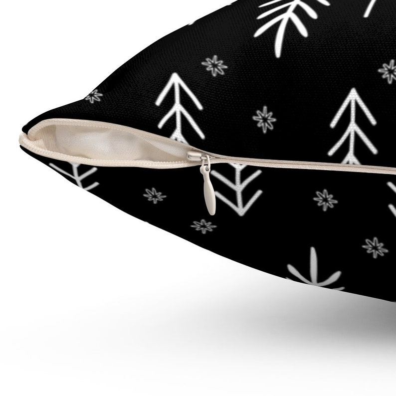 Puede incluir: Coj&iacute;n negro con un patr&oacute;n geom&eacute;trico blanco de &aacute;rboles estilizados y copos de nieve.