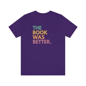 May include: Purple t-shirt with the text "THE BOOK WAS BETTER." in rainbow colors.