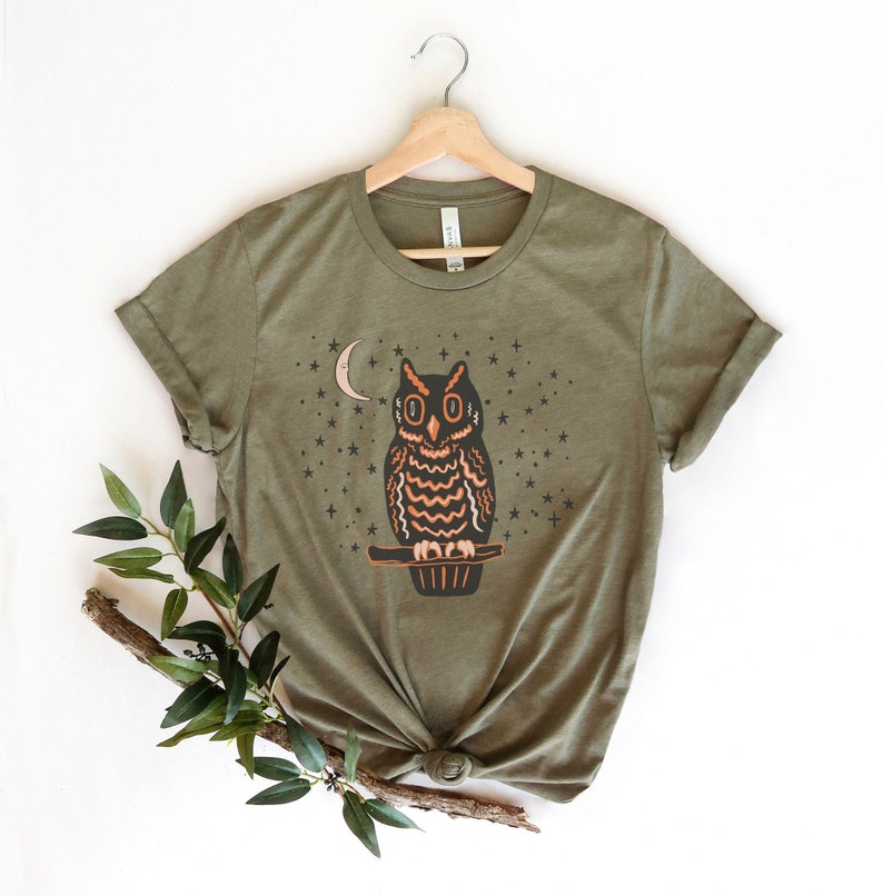 May include: A green t-shirt with a graphic of an owl perched on a branch with a crescent moon and stars in the background.