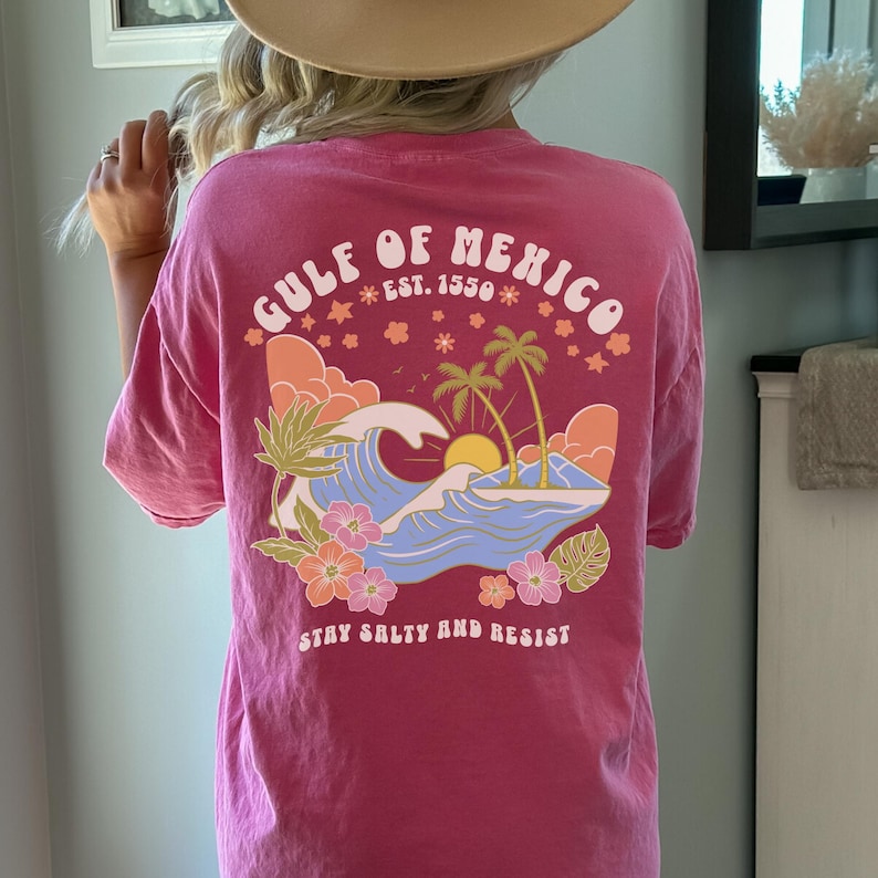 May include: Pink t-shirt with a graphic of a sunset over a wave with palm trees and the text "Gulf of Mexico Est. 1550" and "Stay Salty and Resist".