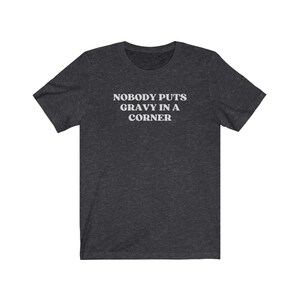 May include: Dark heather gray t-shirt with white text that reads "Nobody puts gravy in a corner".
