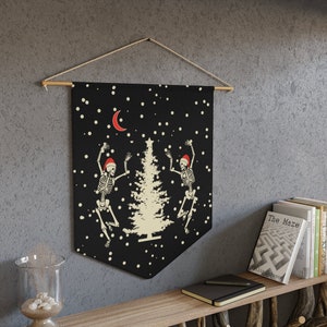 May include: Black tapestry wall hanging featuring two skeletons wearing Santa hats dancing around a white Christmas tree. The background is black with white snowflakes and a crescent moon.
