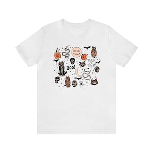 May include: White t-shirt with a black and orange Halloween print featuring cats, owls, pumpkins, skulls, bats, snakes, and the text "Trick or Treat" and "Boo!"