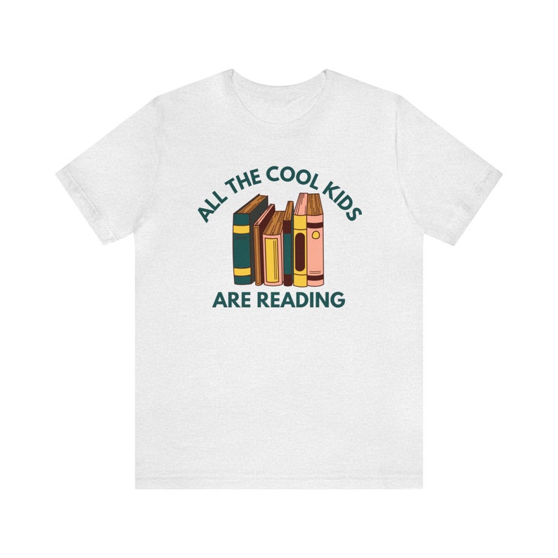 Puede incluir: Camiseta blanca con el texto "All the cool kids are reading" y una pila de libros coloridos.
