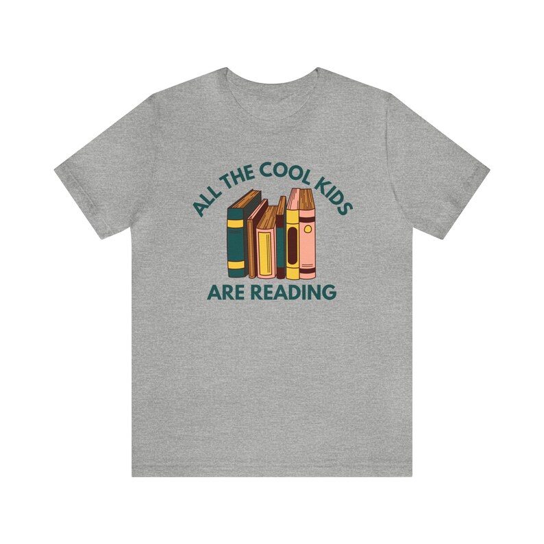 Puede incluir: Camiseta gris con el texto "All the cool kids are reading" y una pila de libros coloridos.