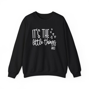 Może przedstawiać: Czarna bluza z okrągłym dekoltem z białym napisem "IT'S THE little things", małymi serduszkami i hasztagiem #NICU. Bluza ma długie rękawy i klasyczny, swobodny styl.